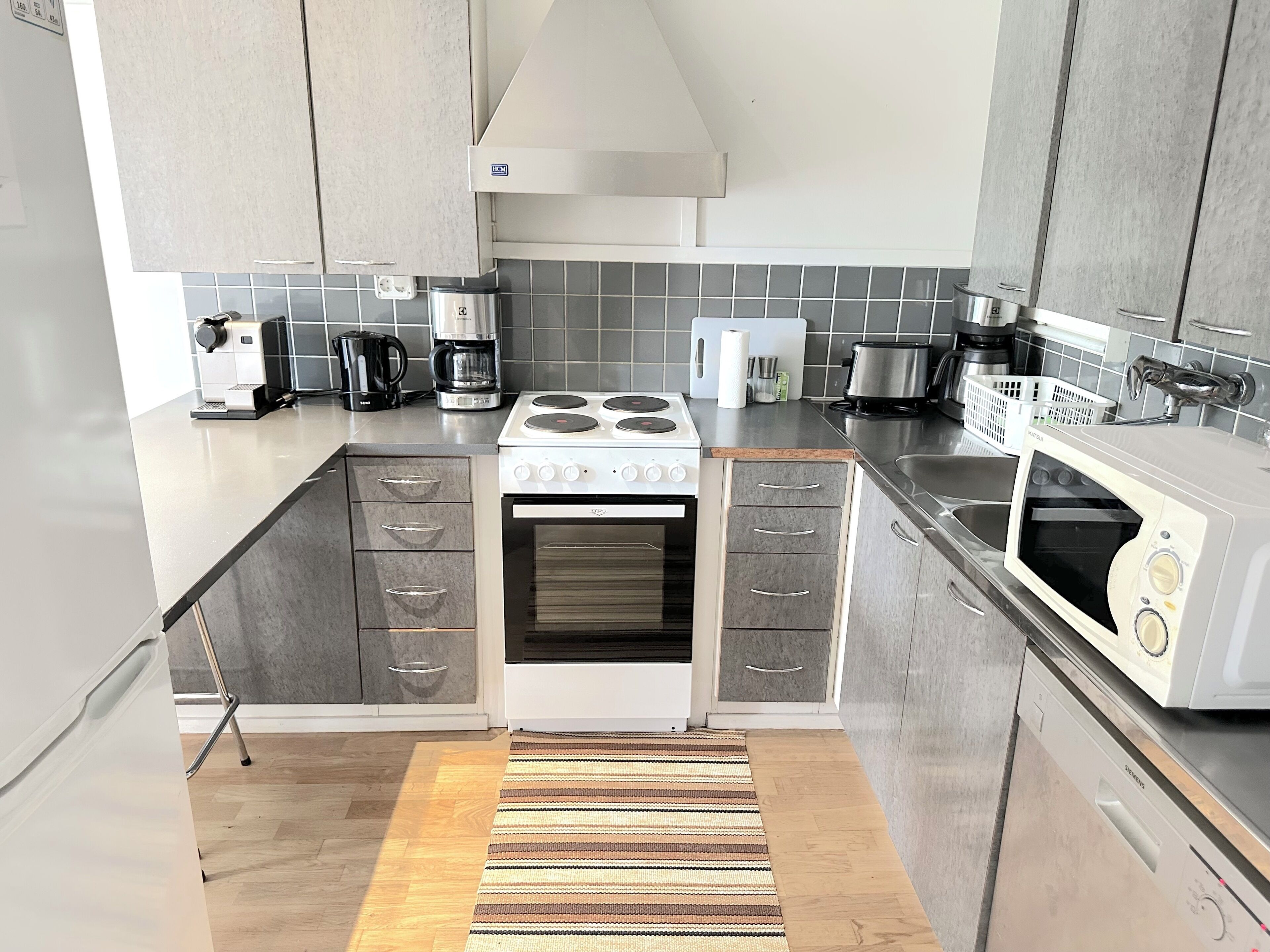 Una cocina moderna con gabinetes grises, estufa, microondas y cafetera.