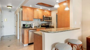 A modern kitchen with wooden cabinets, stainless steel appliances, granite countertops, and a bar area with stools. - New Listing Lahaina Shores 412 Beach Front Resort (Lahaina)