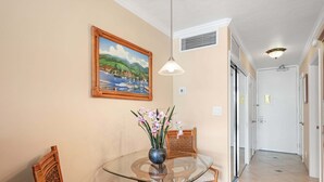 A dining area with a glass table, wicker chairs, a vase with flowers, and a painting on the wall. - New Listing Lahaina Shores 412 Beach Front Resort (Lahaina)