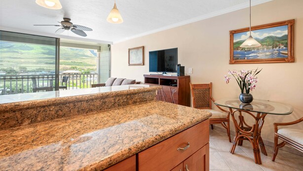 A kitchen with granite countertops, a dining area with a glass table and chairs, a ceiling fan, and a painting on the wall. - New Listing Lahaina Shores 412 Beach Front Resort (Lahaina)
