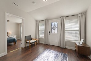 Ein Schlafzimmer mit Bett, Stuhl, Schreibtisch und einem Fenster mit Jalousien.