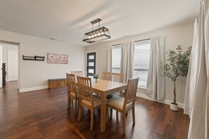 Ein Essbereich mit Holztisch und Stühlen, einer Hängeleuchte, einem Blumentopf und einer Tür mit Fenster.
