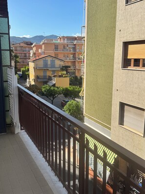 Un balcón con vistas a edificios cercanos, cielo despejado y una montaña distante.