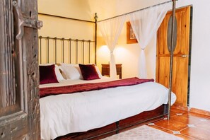 Uma cama com dossel e cortina, uma porta de madeira e um chão de azulejos.