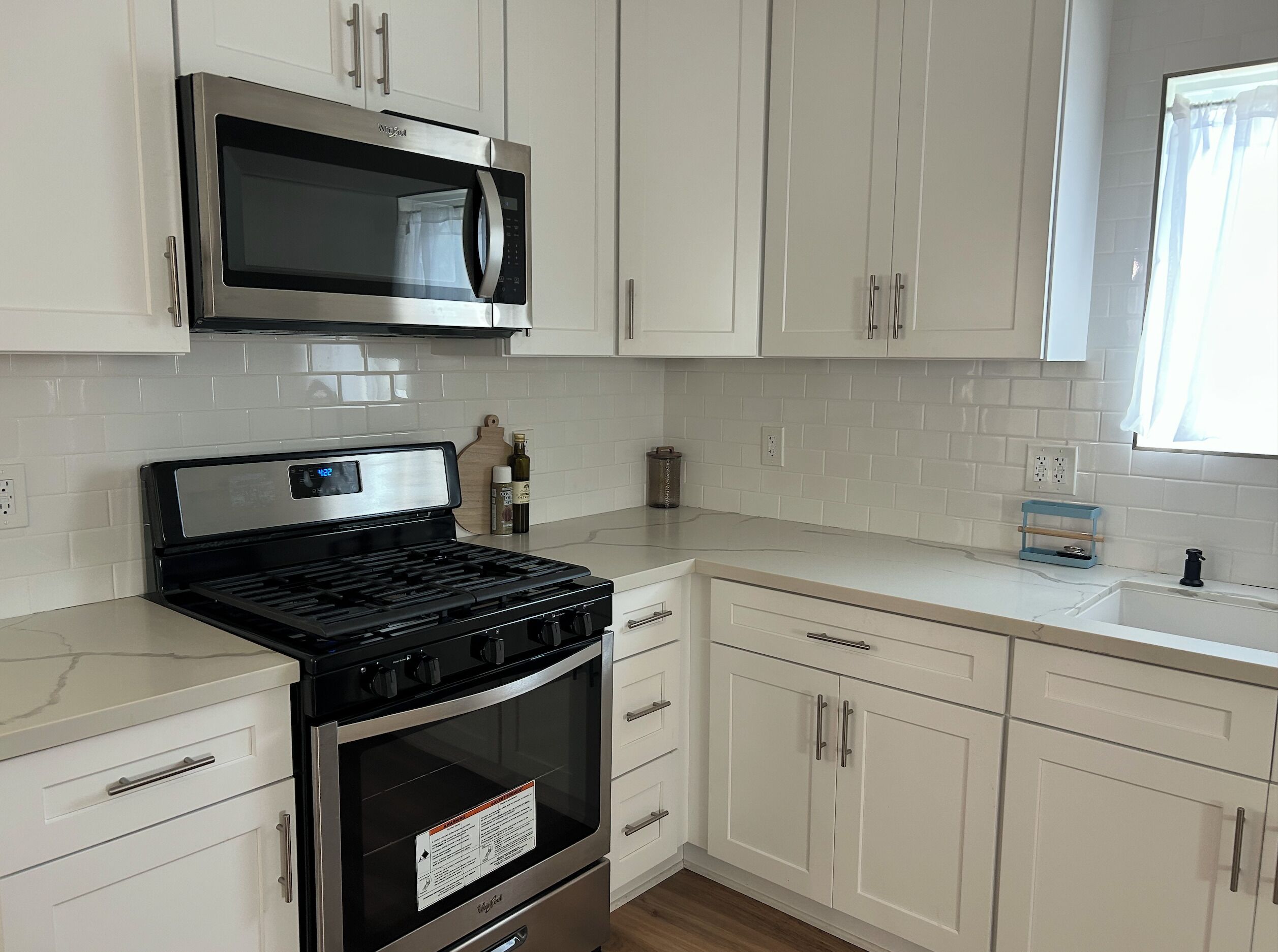 A kitchen with white cabinets, a stainless steel microwave, a gas stove, and a built-in oven.