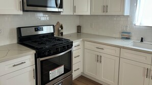 Una cocina con armarios blancos, un microondas de acero inoxidable, una estufa a gas y un horno empotrado.