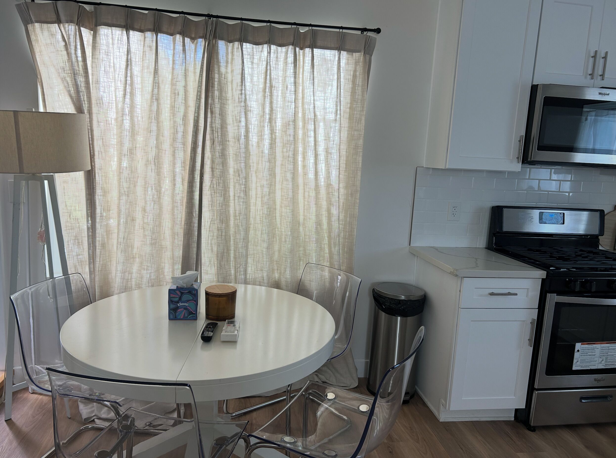 A modern kitchen with a round table, chairs, a microwave, stove, and a trash bin.