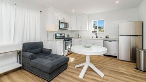 Una cocina moderna con armarios blancos, electrodomésticos de acero inoxidable, una mesa redonda blanca y un sofá gris.