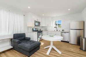 Eine moderne Küche mit weißen Schränken, Edelstahlgeräten, einem runden weißen Tisch und einem grauen Sofa.