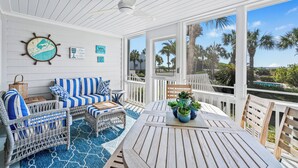 A covered patio with a wooden table, wicker furniture, and a view of palm trees. - Gorgeous Oceanfront Villa, Wild Dunes Resort. Phenomenal Views of Ocean and Community Pool, Unit 56 (Isle Of Palms)