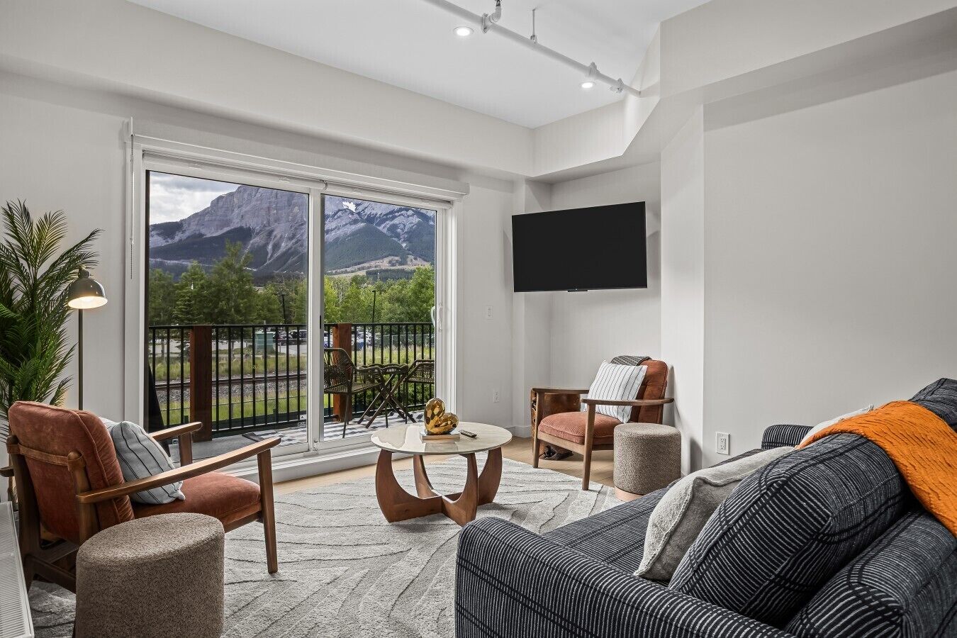 A modern living room with a balcony, a flat-screen TV, and a mountain view.