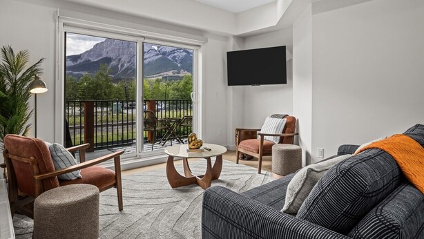 Ein modernes Wohnzimmer mit Balkon, Flachbildfernseher und Blick auf die Berge.