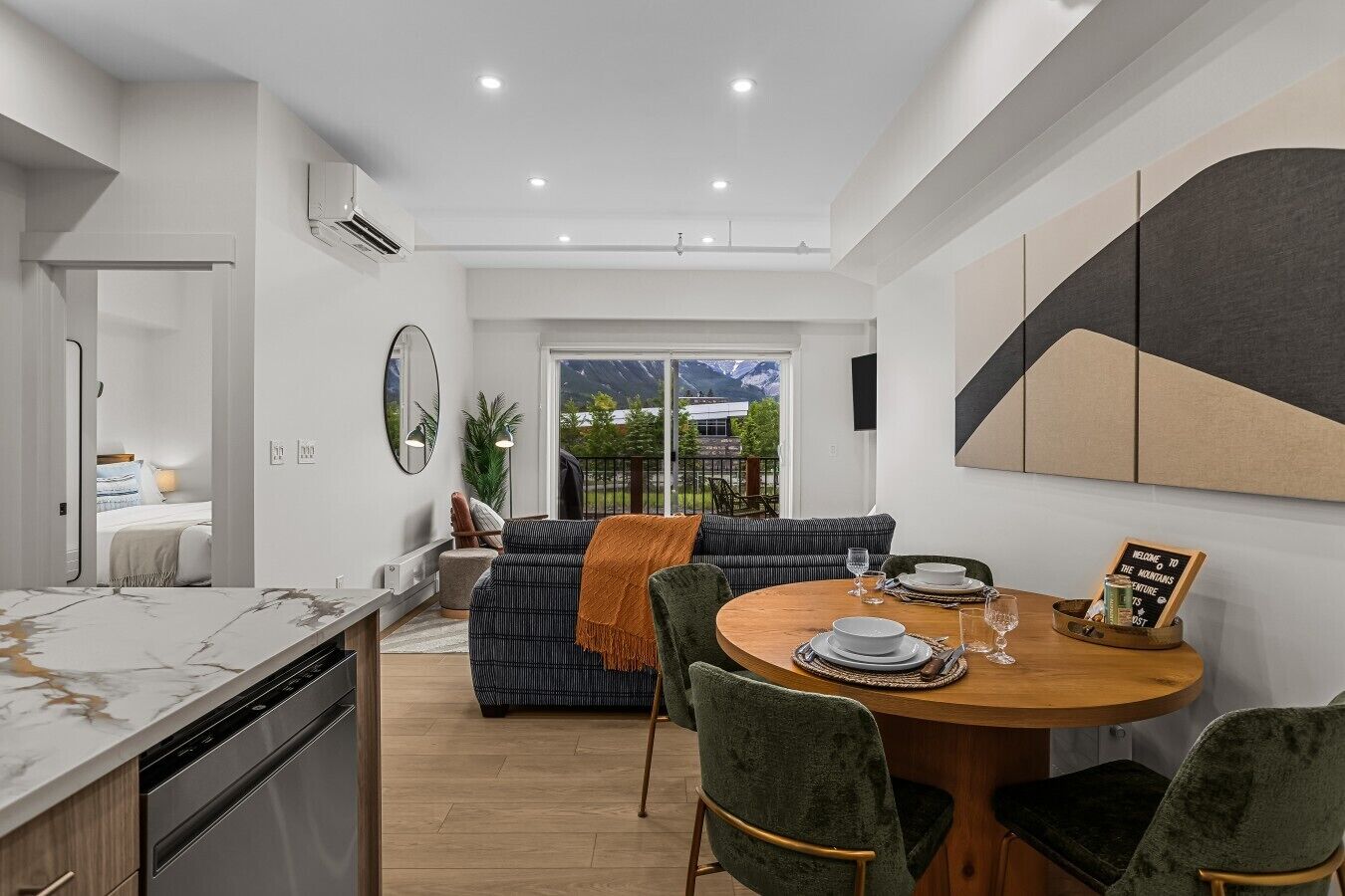 A modern kitchen with a marble countertop, a dining area with a round wooden table, and a view of mountains through the glass door.