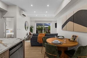 Et moderne køkken med bordplade i marmor, et spiseområde med et rundt træbord, og udsigt til bjerge gennem glasdøren.