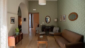 A living room with a sofa, armchairs, a coffee table, a TV stand, and a mirror. There is a plant on a side table and framed pictures on the wall. - Casa Vayu-Rooms and Garden-Rione Sanità (Naples)