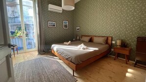 A bedroom with a bed, a window, a bedside table, and a wall-mounted air conditioner. - Casa Vayu-Rooms and Garden-Rione Sanità (Naples)