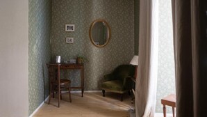 A room with patterned wallpaper, a wooden desk with a chair, a green armchair, and a mirror on the wall. - Casa Vayu-Rooms and Garden-Rione Sanità (Naples)