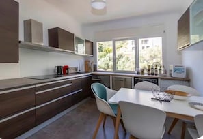 A modern kitchen with a dining area, large windows, and a view of greenery outside. - T4 apartment with incredible views! Sea view, route des sanguinaires (Ajaccio)