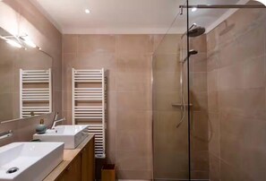 Ein modernes Badezimmer mit einer Duschkabine aus Glas, zwei Waschbecken, einem Handtuchhalter und einem Spiegel.