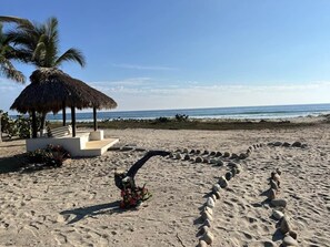A beach with a thatched structure, a winding stone path, and a flower arrangement. - Casa Fuente Ocean Villa (Santa María Colotepec)