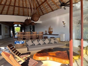 A spacious room with a thatched roof, a sofa set, wooden chairs, and a large wooden table. - Casa Fuente Ocean Villa (Santa María Colotepec)