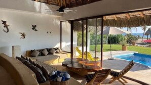 Et moderne indendørs rum med en sofa, et spisebord og en pool udenfor.