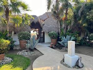 A tropical garden with thatched-roof structures, potted plants, and a central pathway. - Casa Fuente Ocean Villa (Santa María Colotepec)