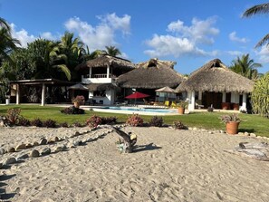 Ein Resort mit strohgedeckten Gebäuden, einem Pool und tropischer Bepflanzung.
