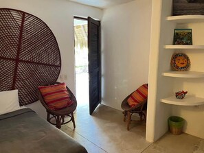 Ein Zimmer mit einem Bett, zwei Korbstühlen mit bunten Kissen, einem großen runden Wandbehang und einem Regal mit Dekoration.