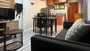 En kompakt opholdsstue med sofa, spisebord med stole, fjernsyn, aircondition og et tekøkken.