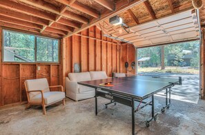 A ping pong table in a room with wooden walls, a sofa, and a window overlooking trees. - Pine & Powder - SHARC, Hot Tub, Bikes, EV Charger (Sunriver)