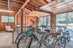 A covered bike storage area with multiple bicycles, wooden walls, and a window providing a view of the outdoors. - Pine & Powder - SHARC, Hot Tub, Bikes, EV Charger (Sunriver)