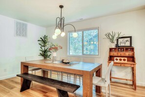 A dining area with a wooden table, bench, chairs, a pendant light, a window with a view, and a wooden cabinet with decorative items. - Pine & Powder - SHARC, Hot Tub, Bikes, EV Charger (Sunriver)
