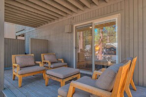A covered outdoor seating area with wooden chairs and a glass door leading to a patio. - Pine & Powder - SHARC, Hot Tub, Bikes, EV Charger (Sunriver)
