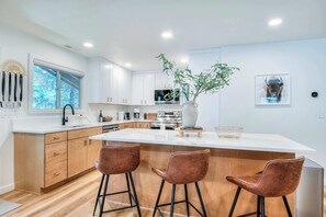 A modern kitchen with a central island, wooden cabinets, and a large window. - Pine & Powder - SHARC, Hot Tub, Bikes, EV Charger (Sunriver)