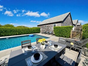 Ein Essbereich am Pool mit einem Tisch für zwei Personen, einem Pool und einem Holzhaus im Hintergrund.