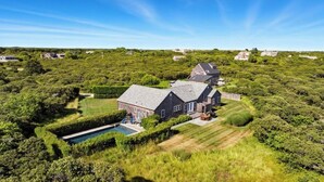 Una casa grande con piscina, rodeada de abundante vegetación y otras viviendas al fondo.