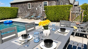 Zona de comedor junto a la piscina con una mesa preparada para cuatro personas, sillas y una piscina.