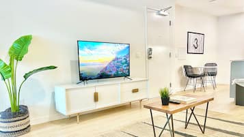 Un saló modern amb televisió de pantalla plana, un armari blanc, zona de menjador amb cadires i una planta en test.