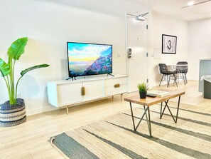 Una sala moderna con un televisor de pantalla plana, un mueble blanco, un comedor con sillas y una planta en maceta.