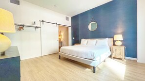 A bedroom with a bed, bedside lamps, a wardrobe, and a mirror on the wall. - Broadway (San Diego)