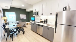 A modern kitchen with stainless steel appliances, a dining area with a table and chairs, and a television. - Broadway (San Diego)
