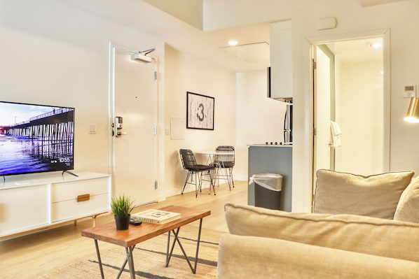 Una sala moderna con un televisor de pantalla plana, un sofá, una mesa de centro y un comedor con sillas y una mesa.
