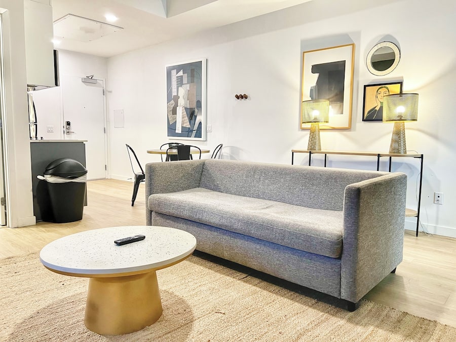 Uma sala de estar moderna com um sofá cinzento, uma mesa de centro redonda e um espaço de jantar com uma mesa pequena e cadeiras.