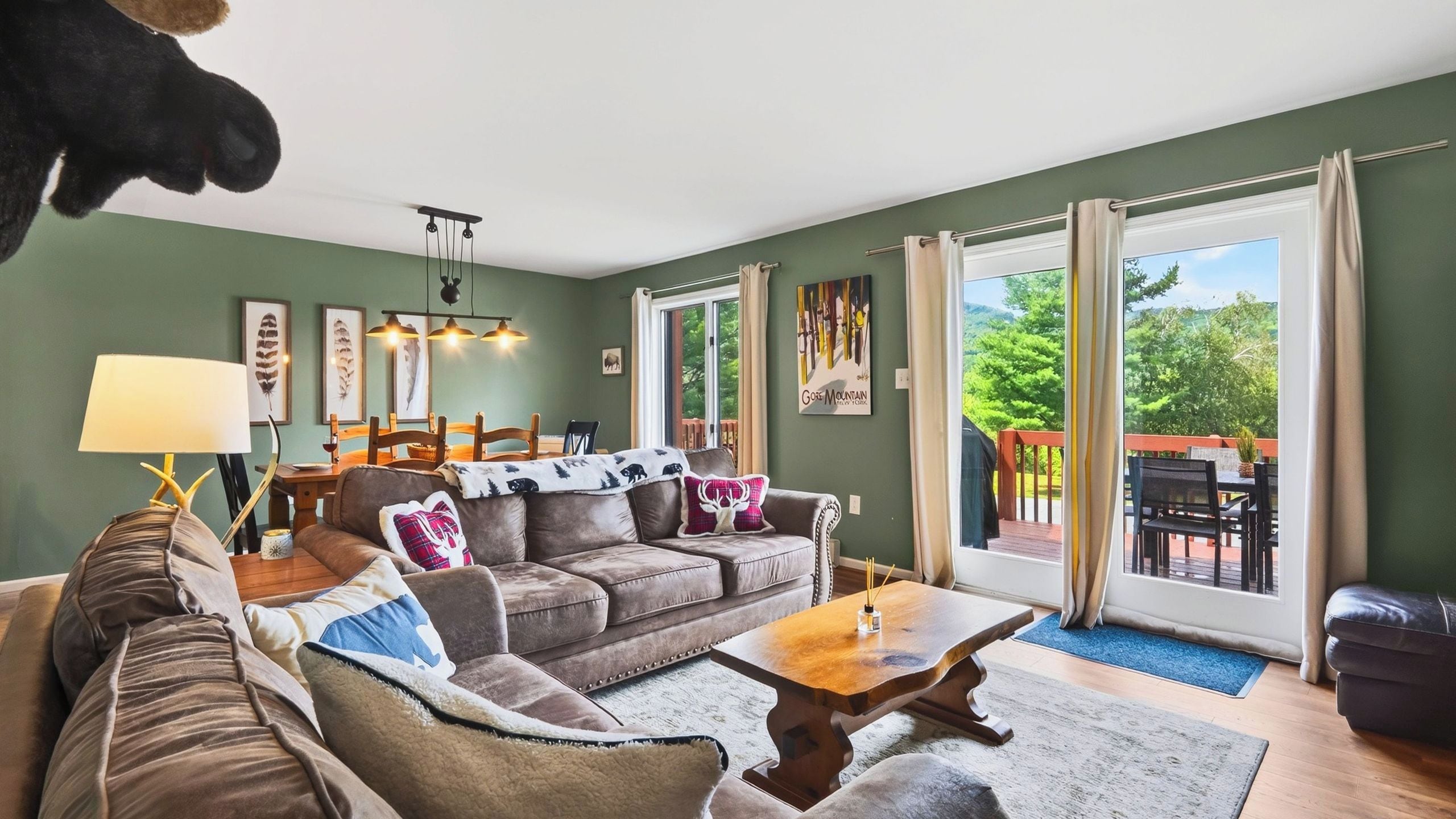 Una sala de estar acogedora con un sofá, sillones, una mesa de centro y una mesa de comedor. Hay cuadros en la pared, una lámpara y vistas al exterior a través de la ventana.