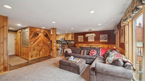 A cozy living room with a fireplace, a dining area, and a kitchen with wooden cabinets. - Lies by Avantstay Indoor Heated Pool + Game Lounge Pool Table + Foosball (North Creek)