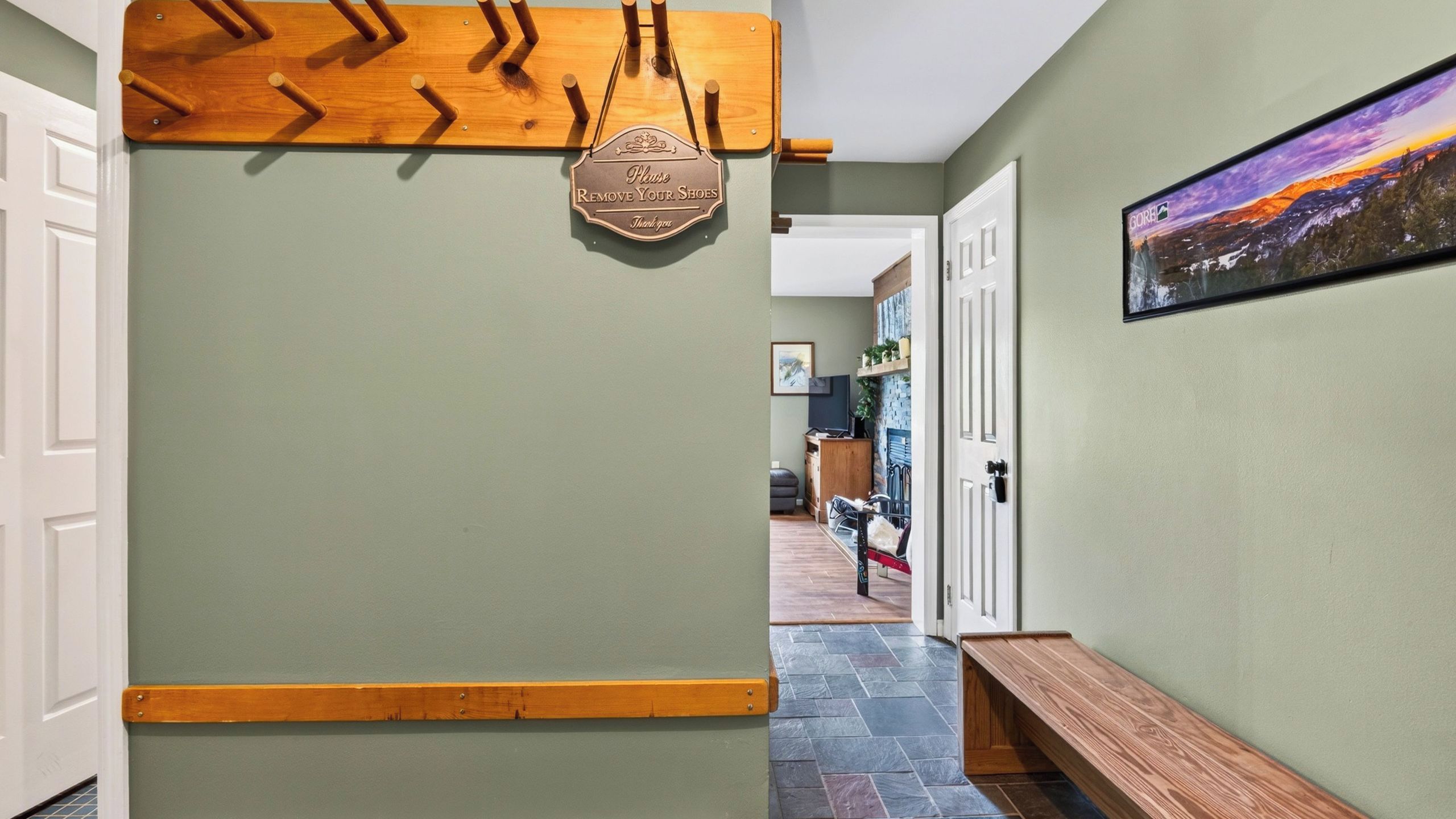 A hallway with a shoe rack, a sign instructing to remove shoes, a bench, and a door leading to another room.