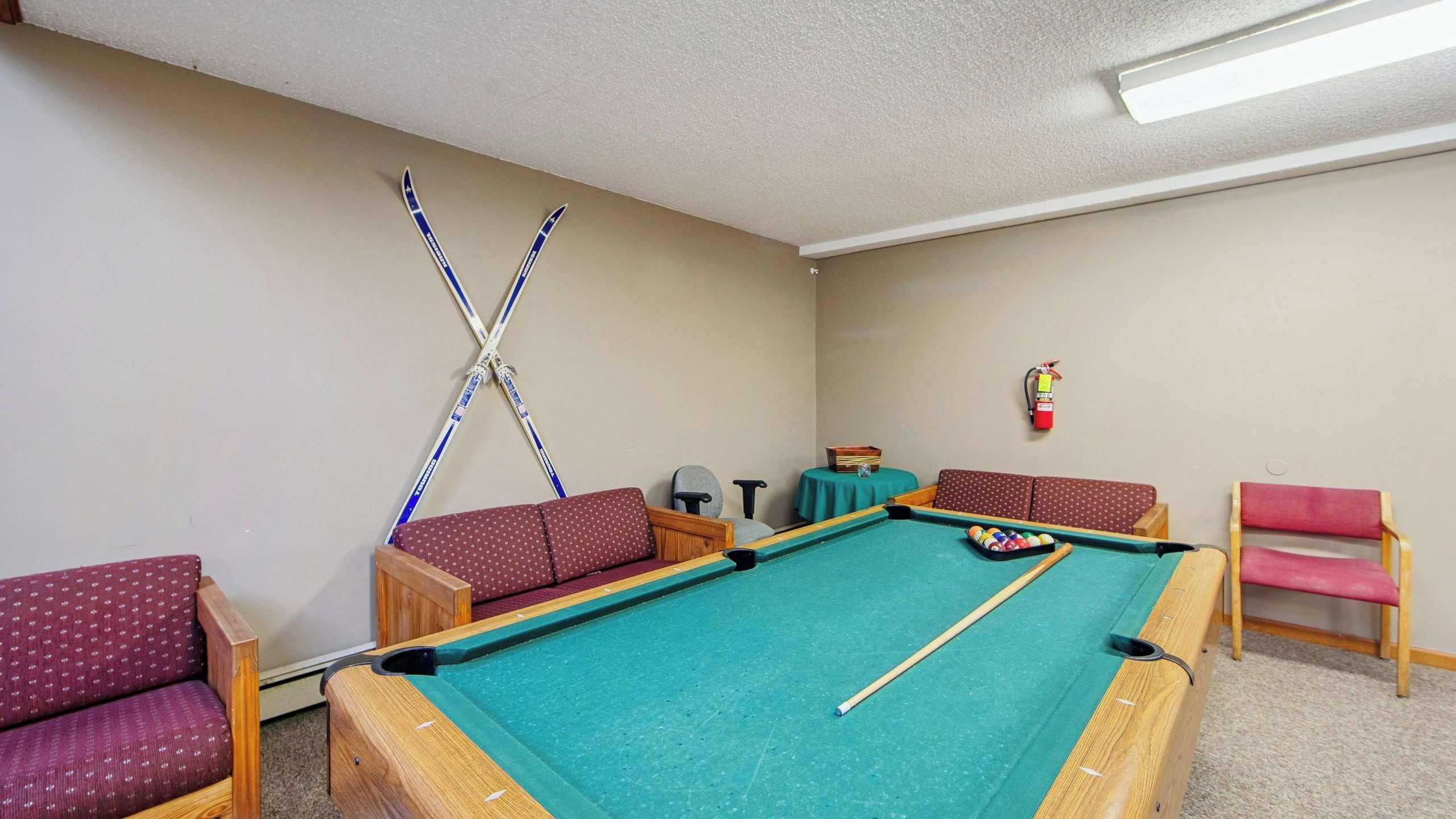 A pool table with cues, a fire extinguisher, and seating.