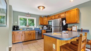 A kitchen with wooden cabinets, a stainless steel refrigerator, a built-in oven, and a window with a view of greenery. - Lies by Avantstay Indoor Heated Pool + Game Lounge Pool Table + Foosball (North Creek)