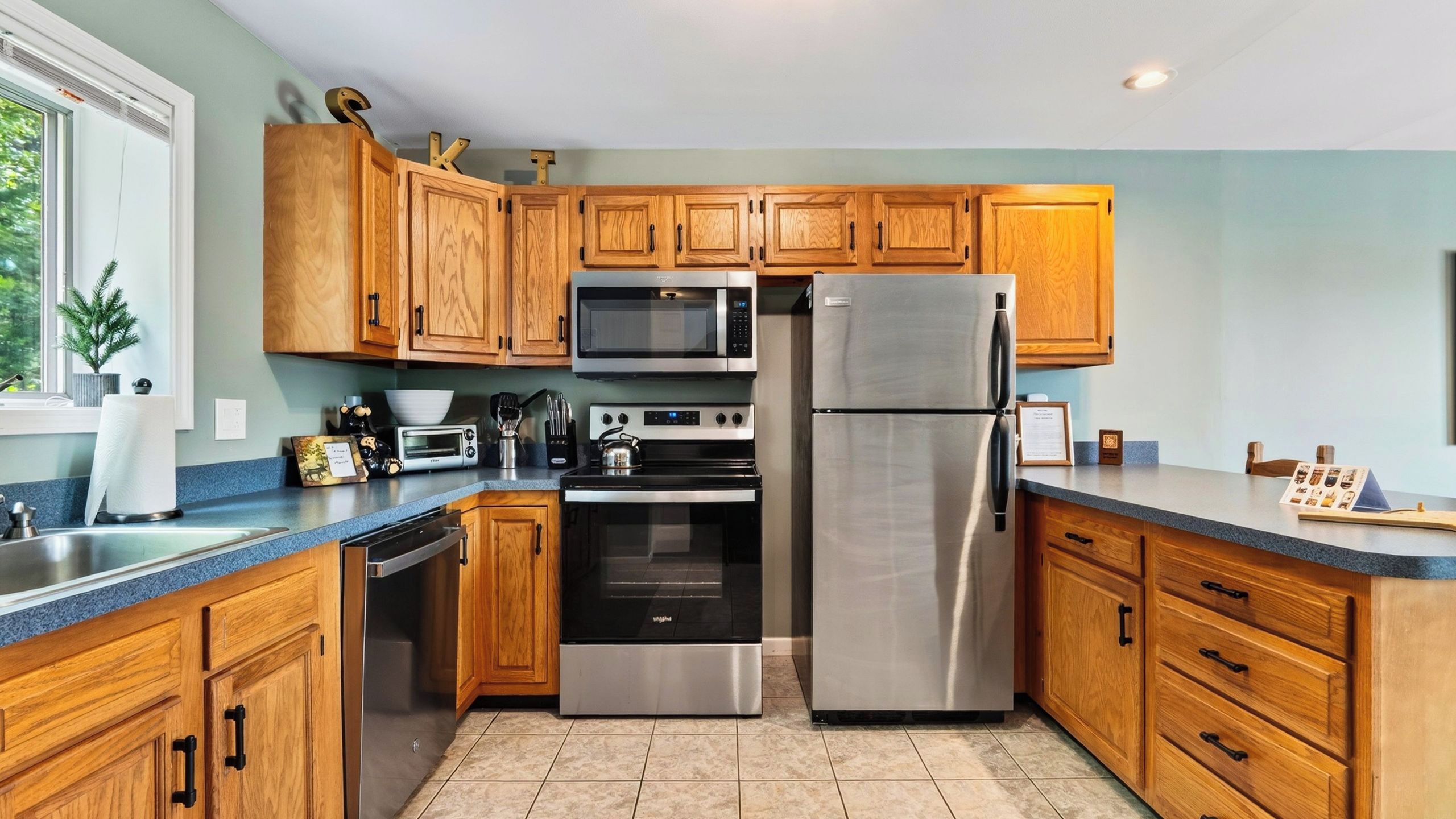 A modern kitchen with wooden cabinets, stainless steel appliances, and a blue countertop.